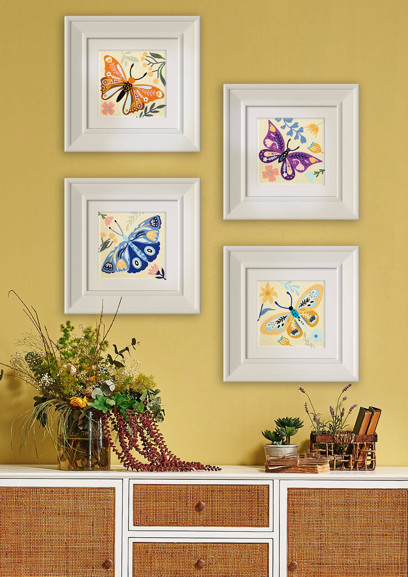 Four framed butterfly artworks on a yellow wall above a wooden cabinet.