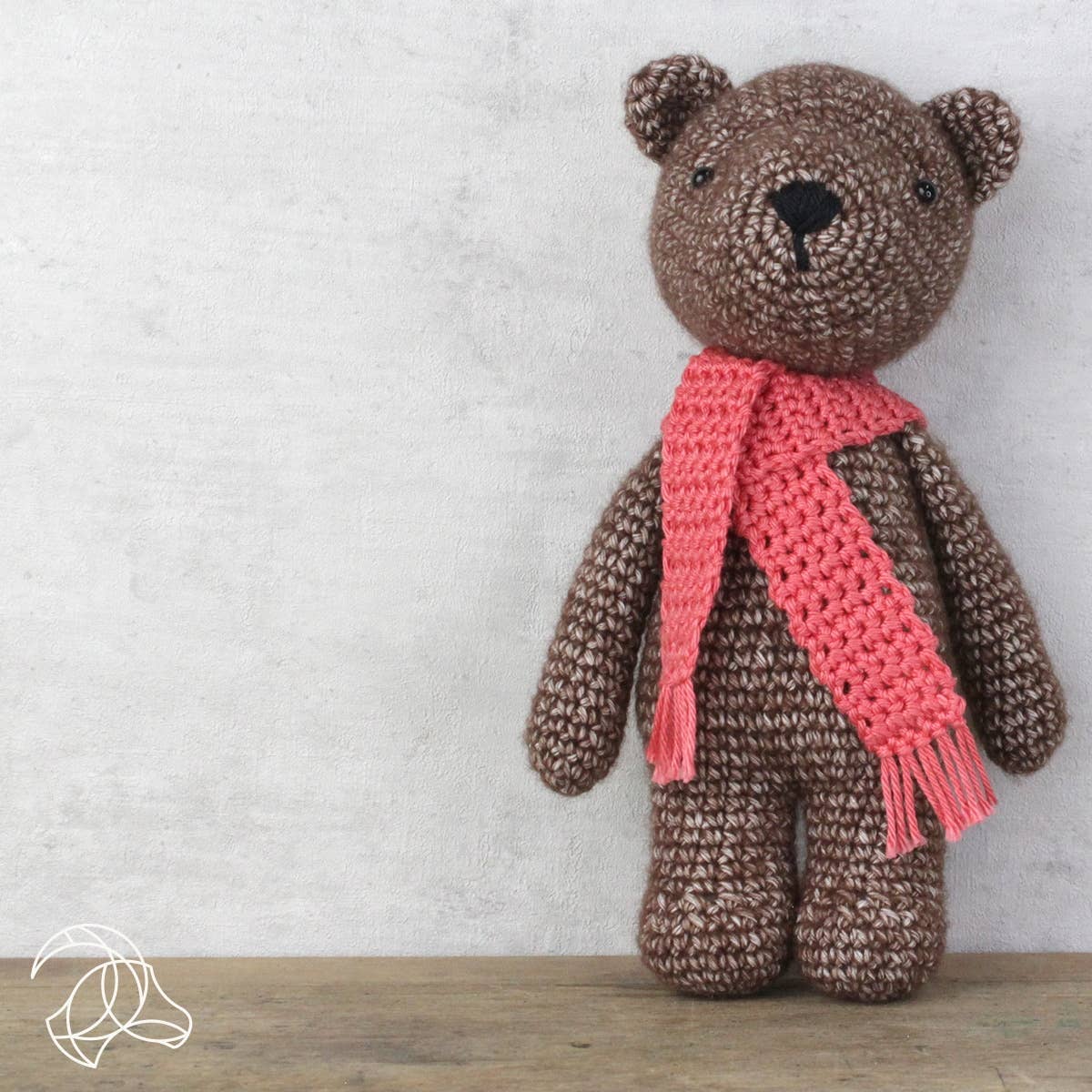 Brown teddy bear with a pink scarf on a light gray background