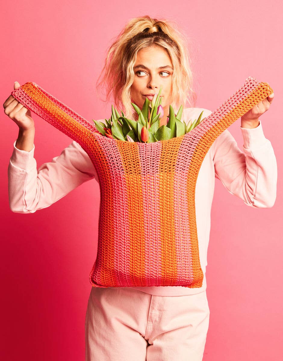 Person holding a colorful knitted bag with tulips against a pink background