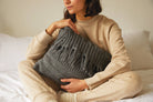 Person holding a gray knitted pillow on a bed