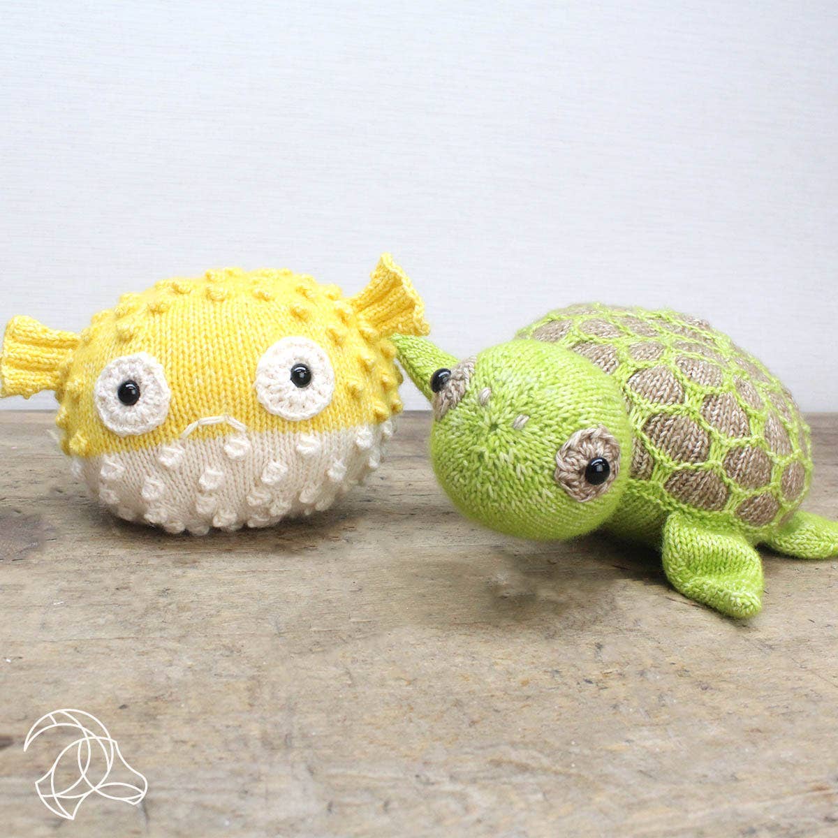 Knitted yellow fish and green turtle toy on a wooden surface with a light gray background
