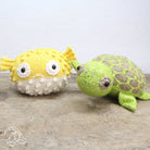 Knitted yellow fish and green turtle toy on a wooden surface with a light gray background