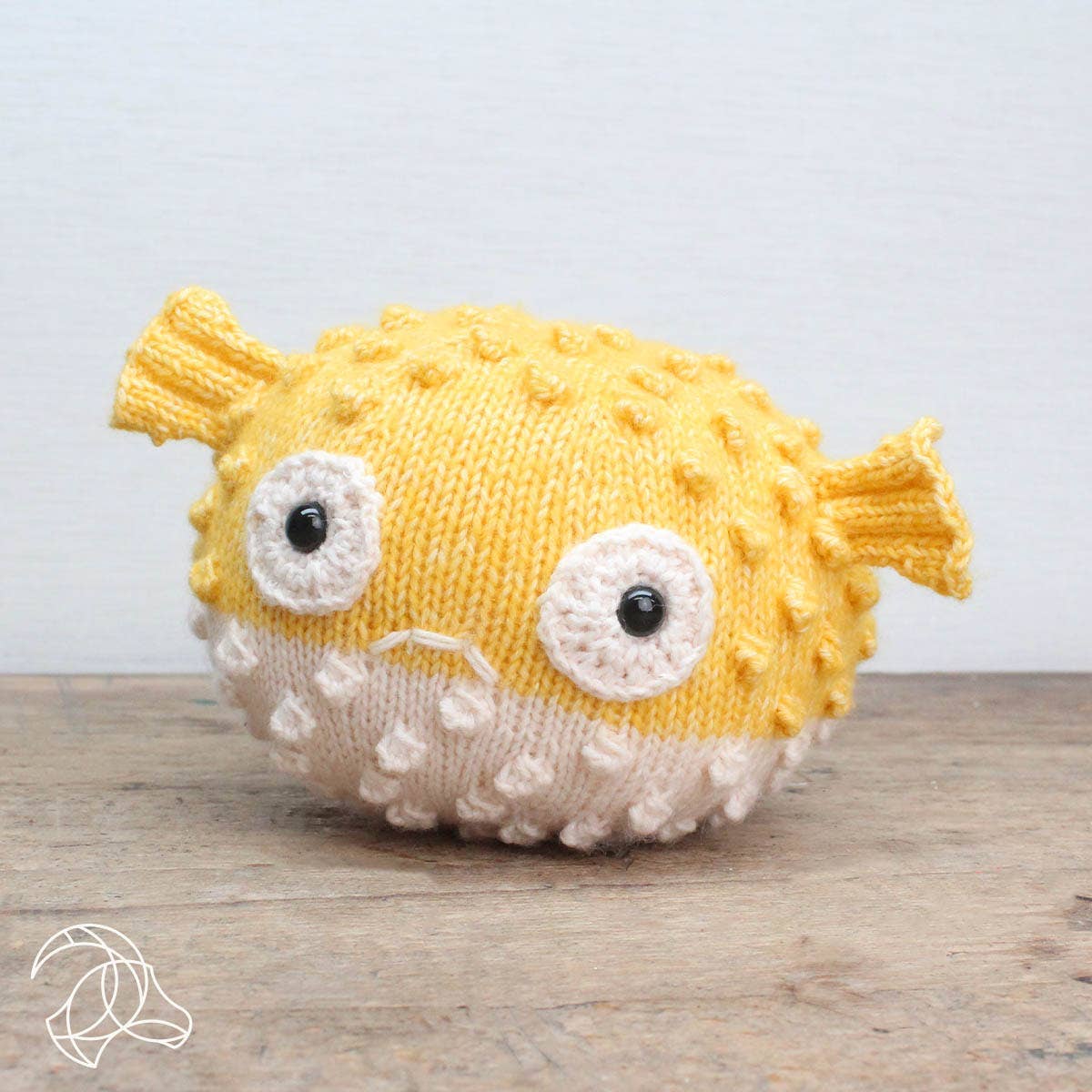 Knitted yellow and white fish toy on a wooden surface with a light gray background
