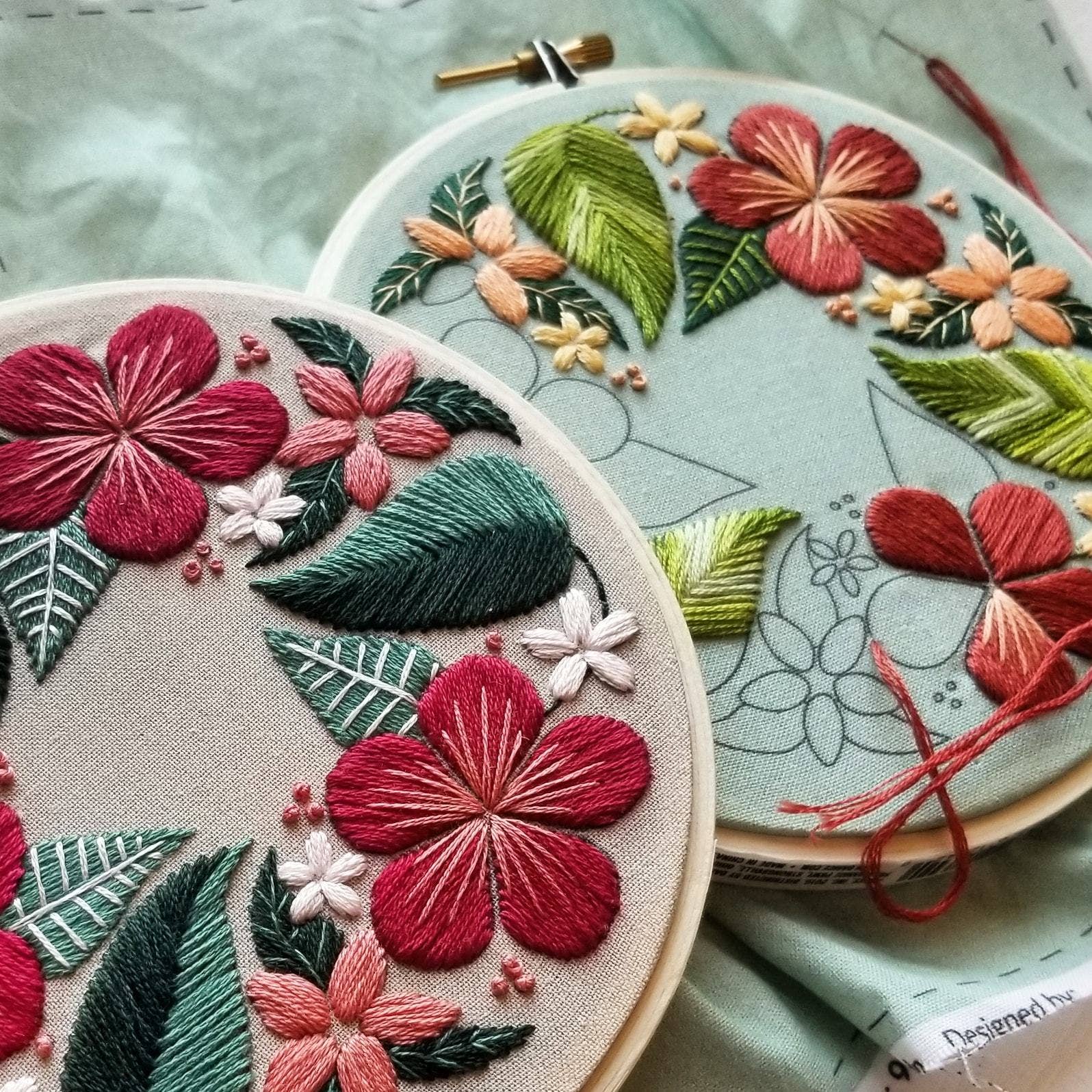 Two embroidery hoops with floral patterns on a light green fabric background.