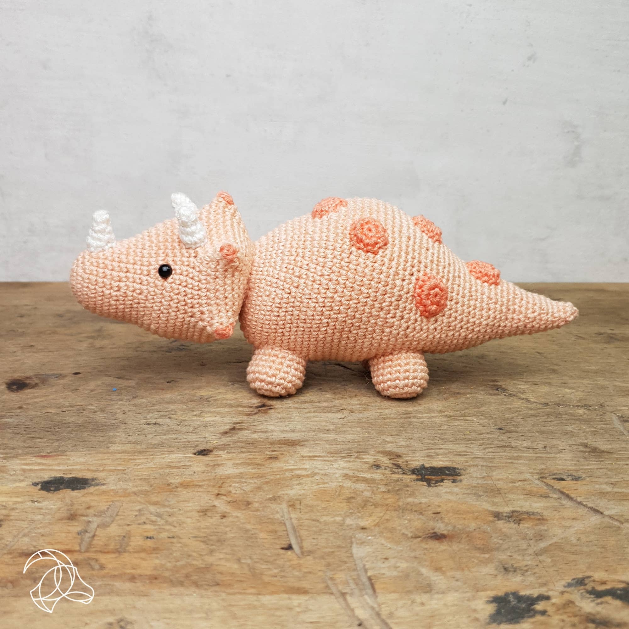 Crocheted triceratops dinosaur toy on a wooden surface with a gray background