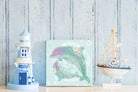 Decorative items including a lighthouse, a sailboat, and a dolphin painting on a wooden surface with a light blue wooden panel background.