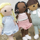 Three knitted dolls with different hair colors and outfits on a wooden surface.