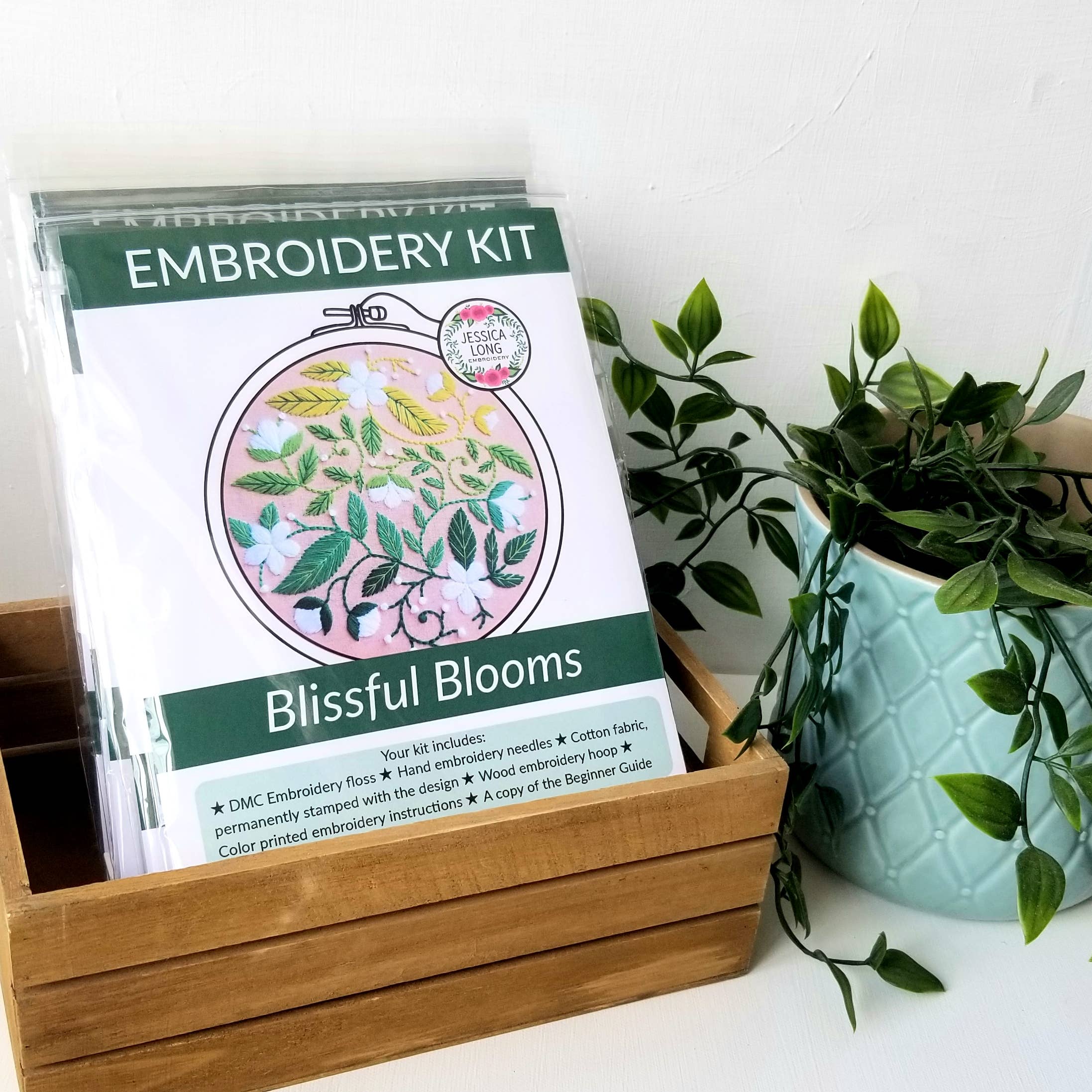 Embroidery kit with 'Blissful Blooms' design on a white surface with a plant.
