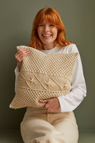 Woman holding a woven beige pillow against a plain background