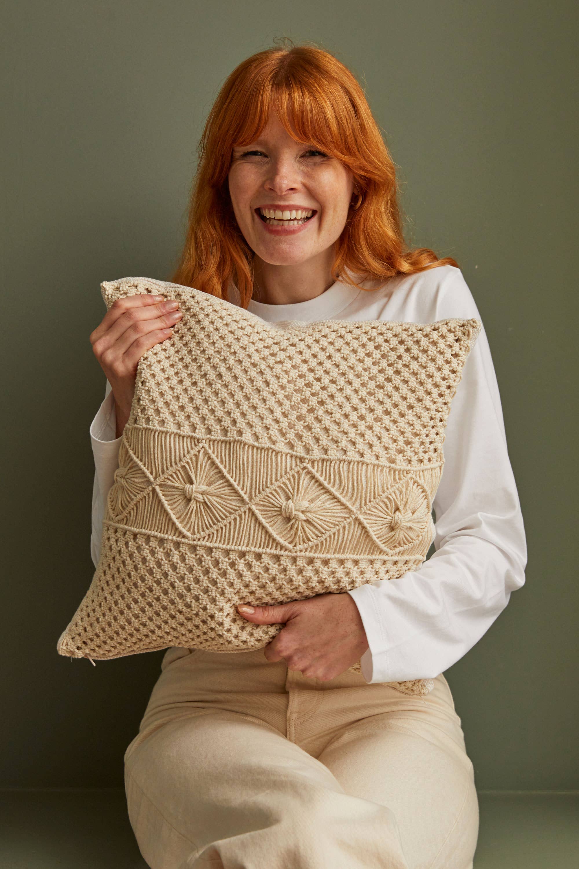 Woman holding a woven beige pillow against a plain background