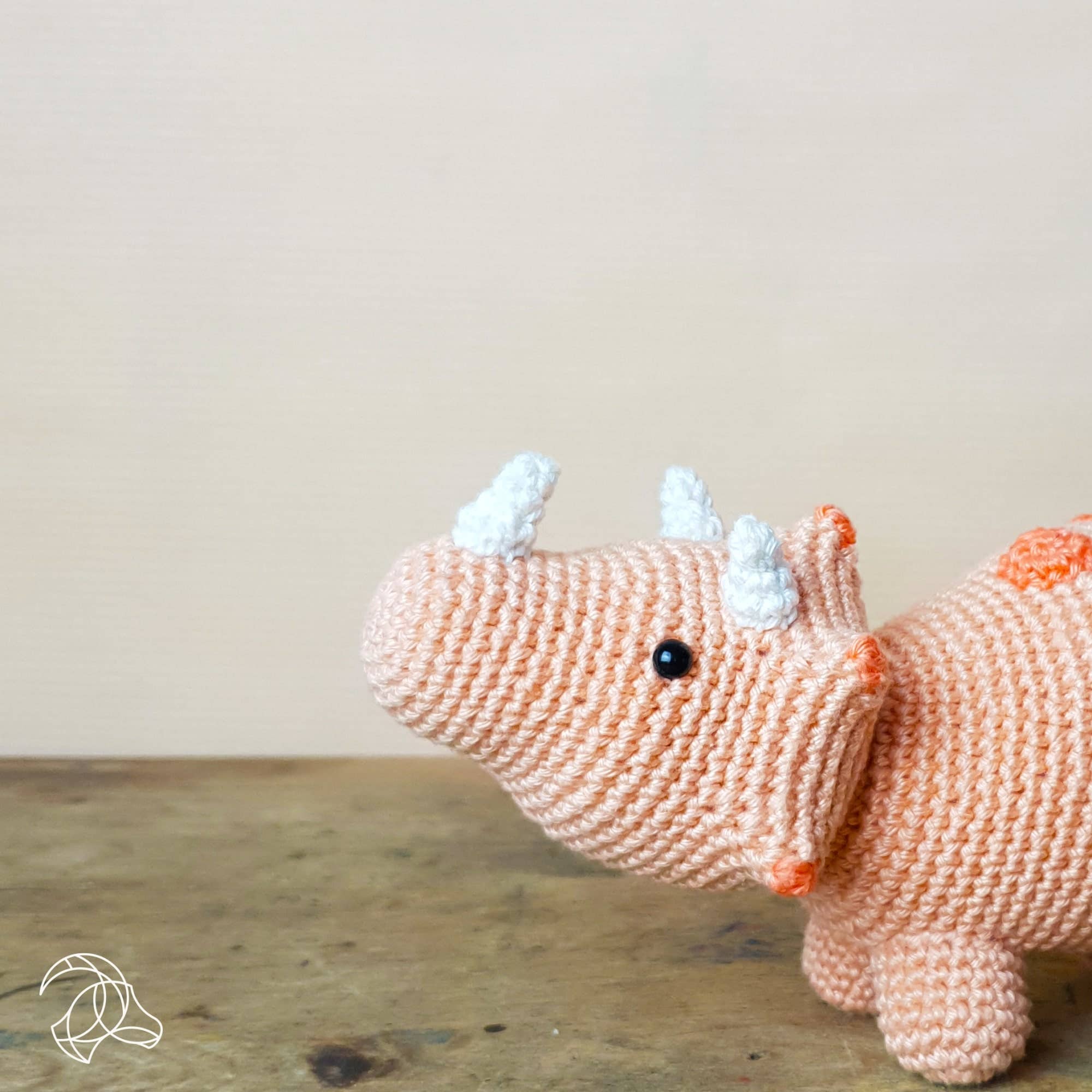 Knitted rhino toy on a wooden surface with a plain background