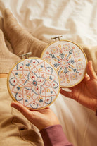 Two hands holding embroidery hoops with floral patterns on a soft beige background