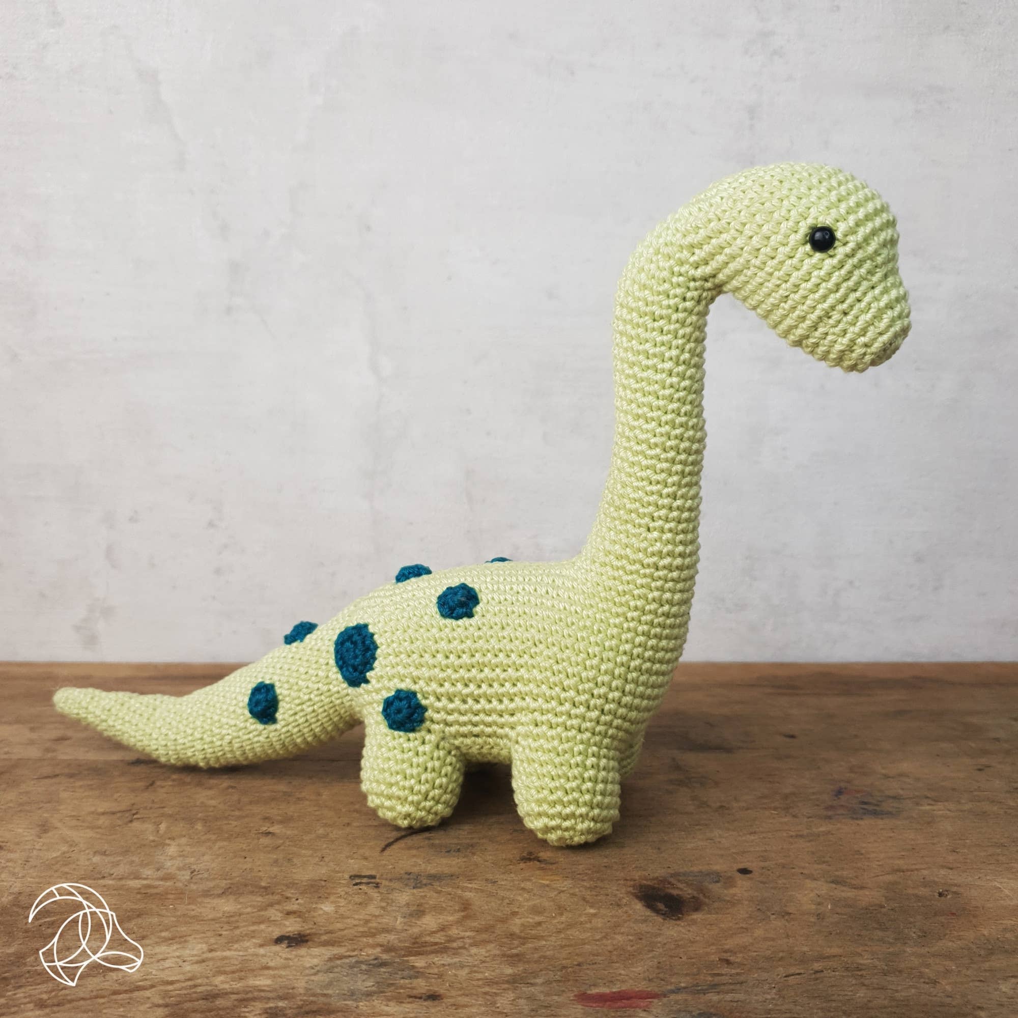 Crocheted dinosaur toy on a wooden surface with a light gray background