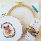 Embroidery hoop with a completed hedgehog design and embroidery kit on a white background
