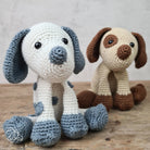 Two crochet dogs, one blue and white with black spots, the other brown and white, on a wooden surface.