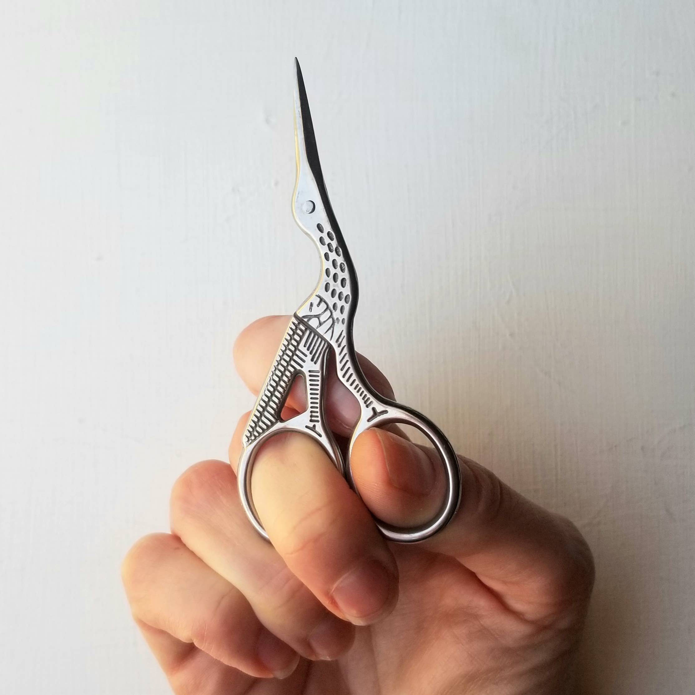 Hand holding a pair of decorative scissors against a plain background