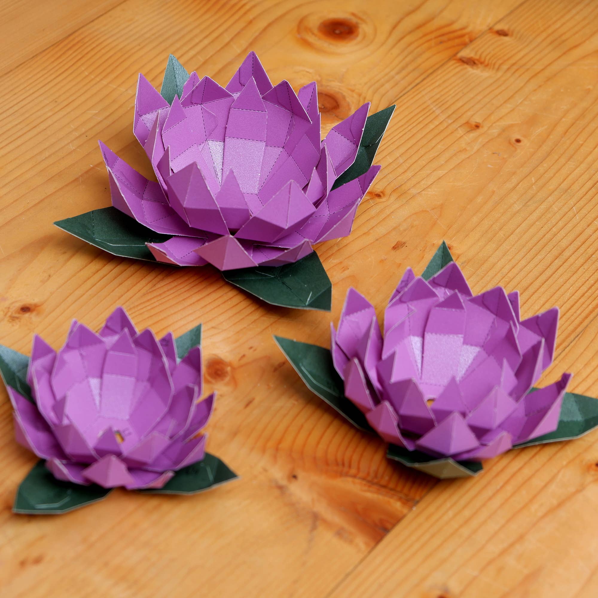 Three purple paper lotus flowers on a wooden surface