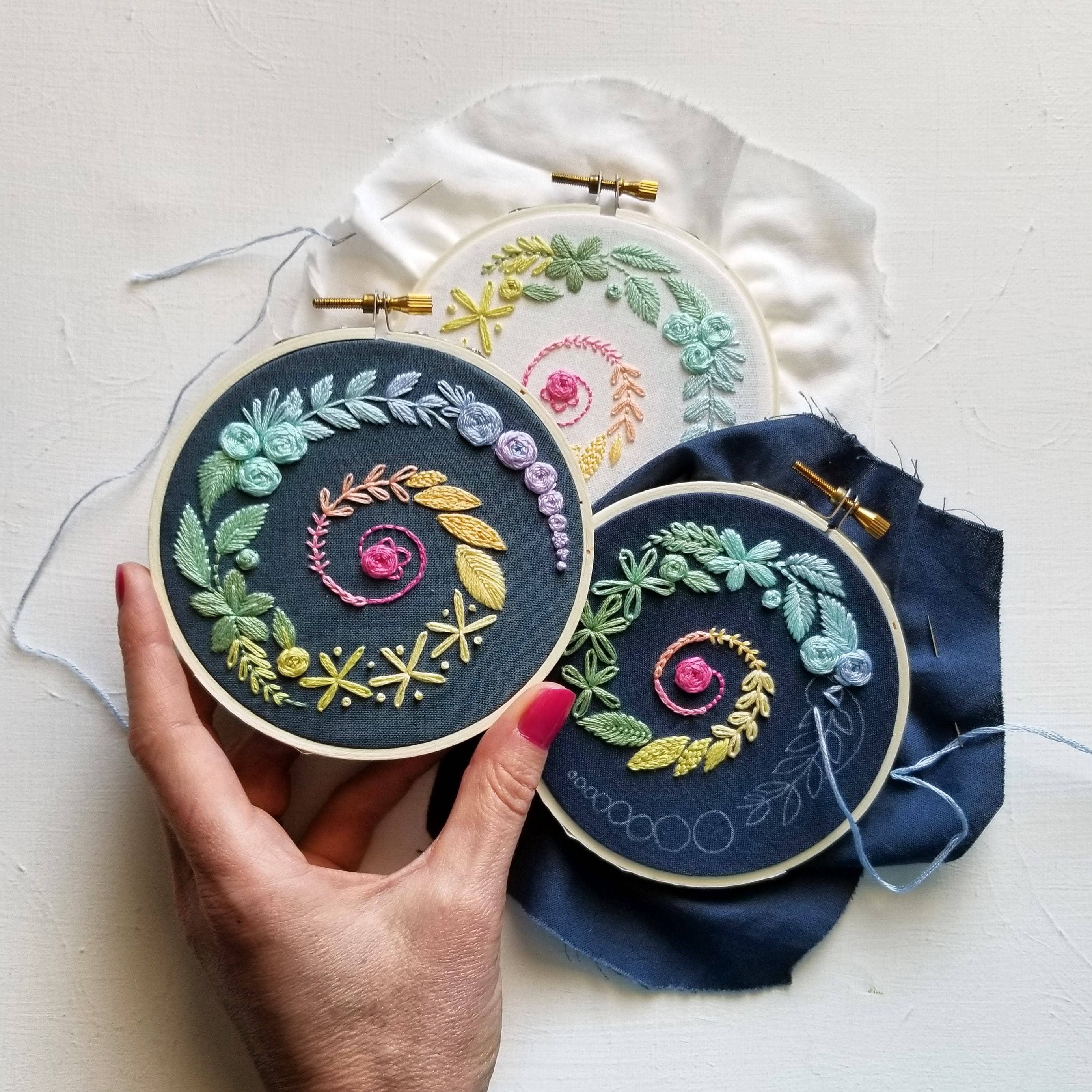 Three embroidered hoops with colorful floral patterns held by a hand on a light background