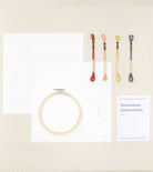 Embroidery hoop, colorful needles, and a paper with text on a beige background