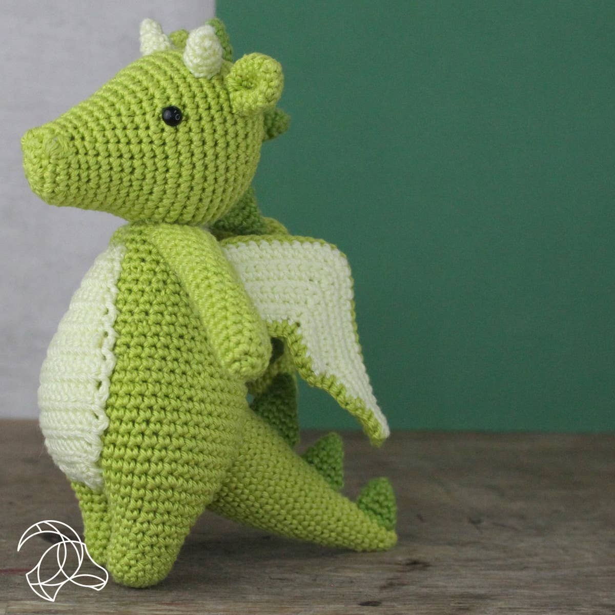 Green crochet dragon toy on a wooden surface with a green wall background