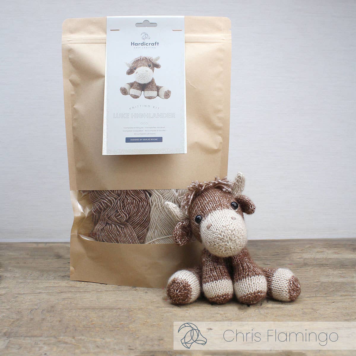 Knitted horse toy next to a brown paper bag with a label on a wooden surface.