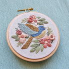 Embroidery hoop with a colorful bird and floral design on a light blue background
