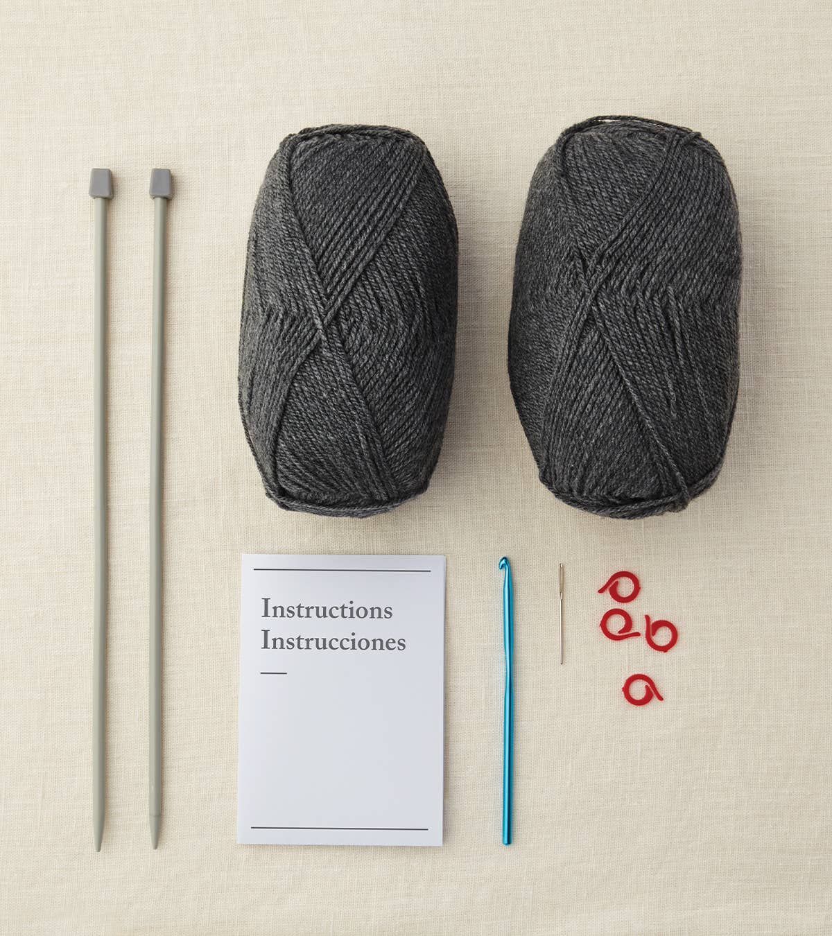 Two balls of gray yarn, knitting needles, a crochet hook, and instructions on a beige surface.