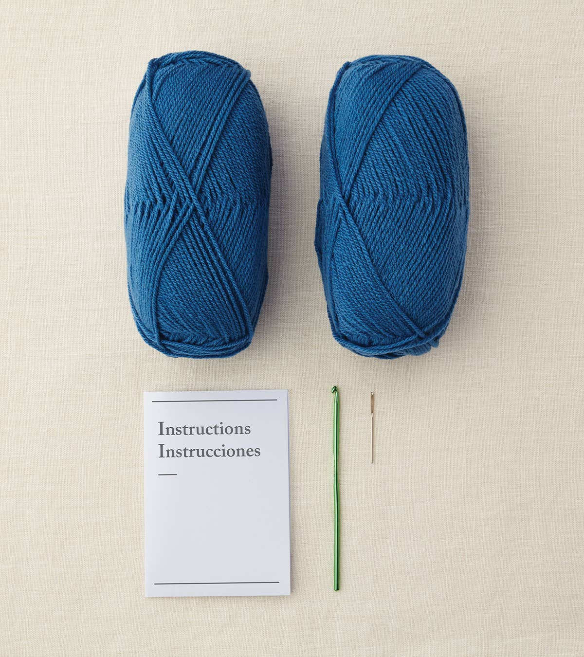 Two blue skeins of yarn with a crochet hook and instructions on a beige surface