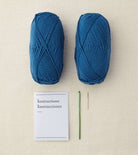 Two blue skeins of yarn with a crochet hook and instructions on a beige surface