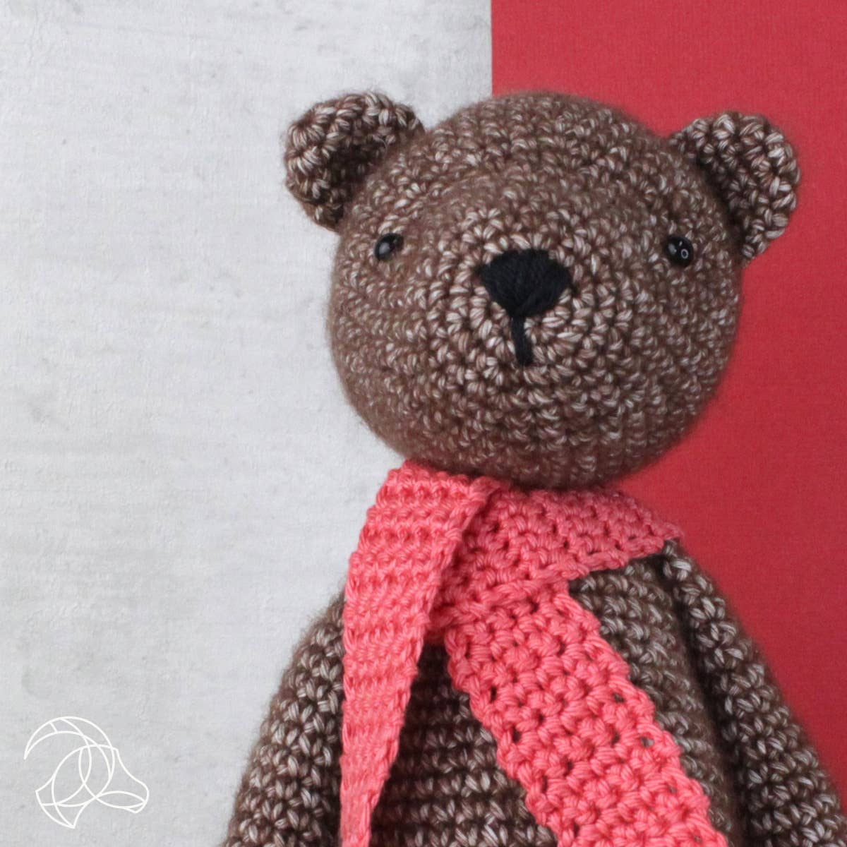 Crocheted teddy bear with a pink scarf on a red and gray background