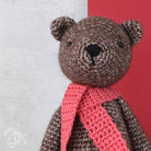 Crocheted teddy bear with a pink scarf on a red and gray background